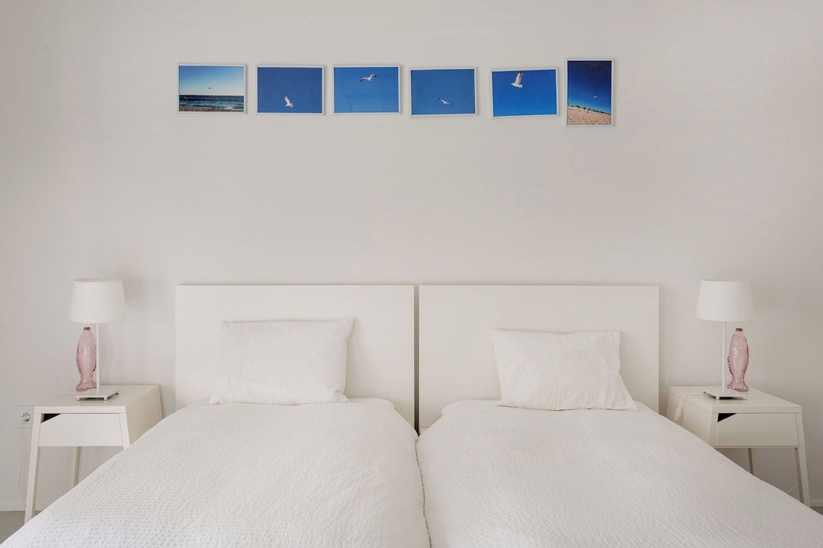 A double bed with white bedding, two bedside tables with lamps, and a wall with five framed pictures.