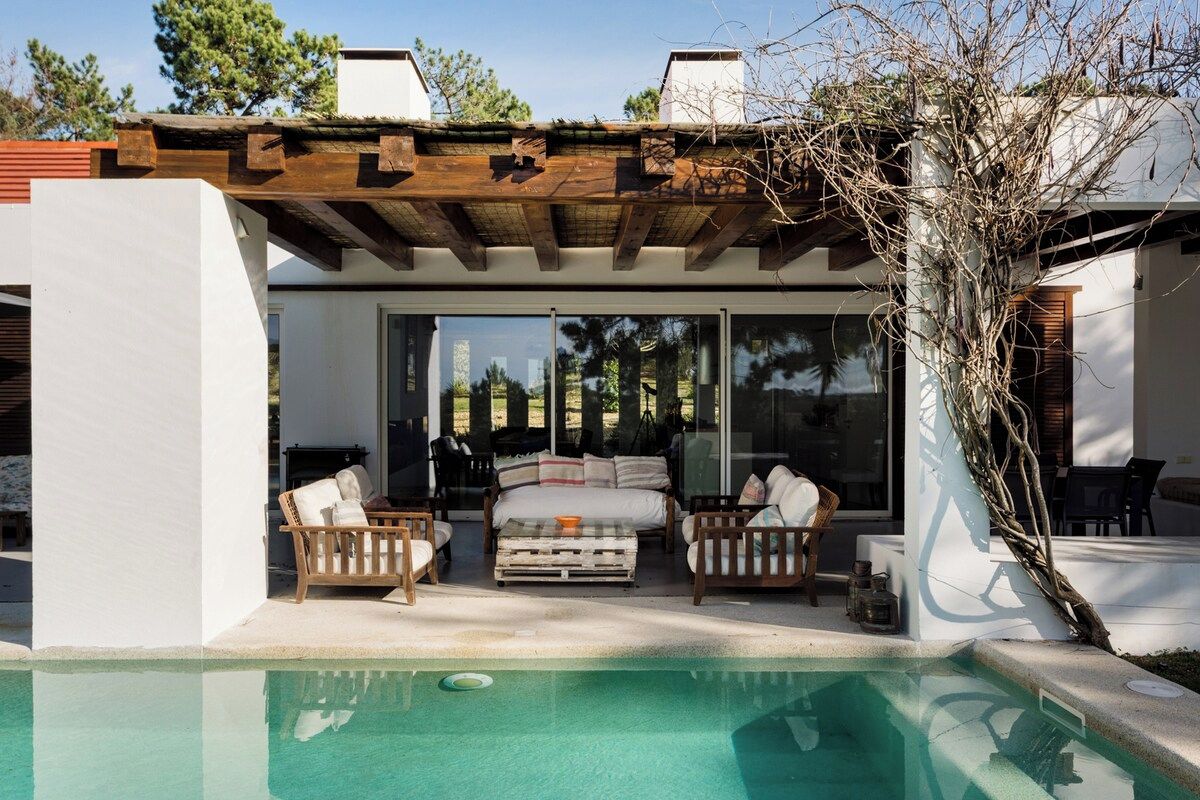 A modern outdoor living area with a pool, wooden furniture, and a pergola.