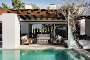 A modern outdoor living area with a pool, wooden furniture, and a pergola. - Casa Glicinias in Comporta (Grandola)