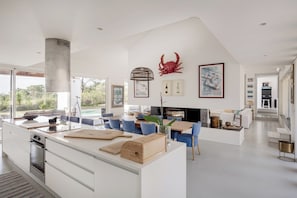 A modern kitchen with a central island, dining area with blue chairs, and a fireplace. - Casa Glicinias in Comporta (Grandola)