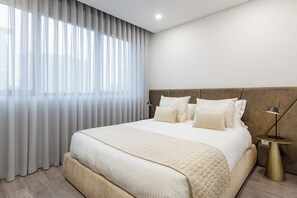 Ein modernes Hotelzimmer mit einem großen Bett, einem Nachttisch und einem Fenster mit durchsichtigen Vorhängen.