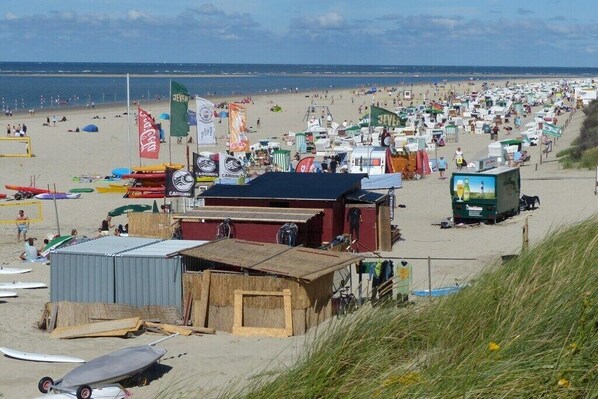 Ein Strand mit vielen Zelten und Sonnensegeln, einem kleinen Gebäude und mehreren Booten.