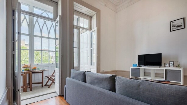 A living room with a grey sofa, a television on a white stand, and a table with fruits and a bowl. - Palazzo Alvares Cabral - Apartamento E (Porto)