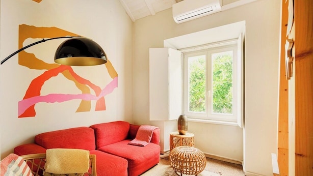 Ein Zimmer mit einem roten Sofa, einer Lampe, einem Fenster und einem Wandbild.