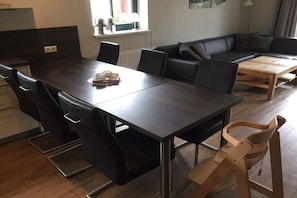 Ein stilvoller Wohnraum mit einem dunklen Esstisch aus Holz, schwarzen Ledersesseln, einem schwarzen Ledersofa und einem Couchtisch aus Holz.