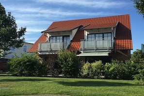 Ein zweistöckiges Haus mit rotem Ziegeldach, einem Balkon im Obergeschoss und einem gepflegten Rasen.