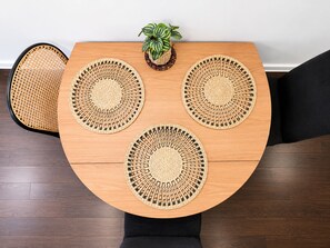 A round wooden table with four woven placemats and a small potted plant. - Modern 2BDR Near Airport and Train Station (Mascot)