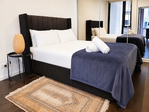 Ein modernes Hotelzimmer mit einem großen Bett, einem Nachttisch mit Lampe, einem gemusterten Teppich und einem großen Spiegel, der den Raum reflektiert.