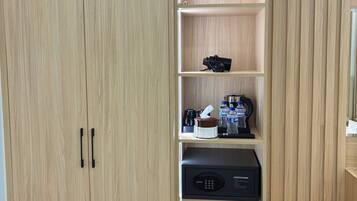 Une armoire en bois à deux portes, une étagère avec un appareil photo, une machine à café, une bouteille d’eau et un petit réfrigérateur.