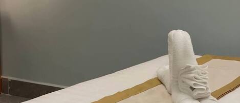 A neatly made bed with a white and gold striped bedspread, a folded white towel, and a folded brown towel.