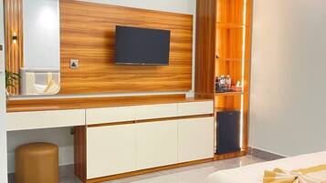 Une chambre d’hôtel moderne équipée d’un lit, d’un téléviseur fixé au mur, d’un minibar et d’une armoire en bois.