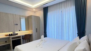 A modern hotel room with a large bed, a desk, a wardrobe, and a large window with curtains.