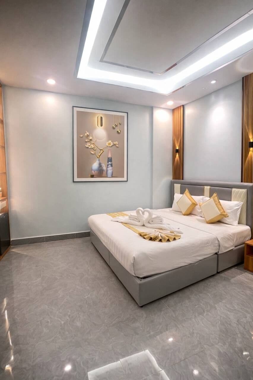 A modern hotel room with a large bed, a ceiling light fixture, and a framed artwork on the wall.