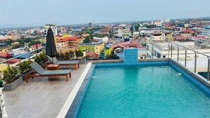 A rooftop swimming pool with lounge chairs and an umbrella, surrounded by a cityscape.