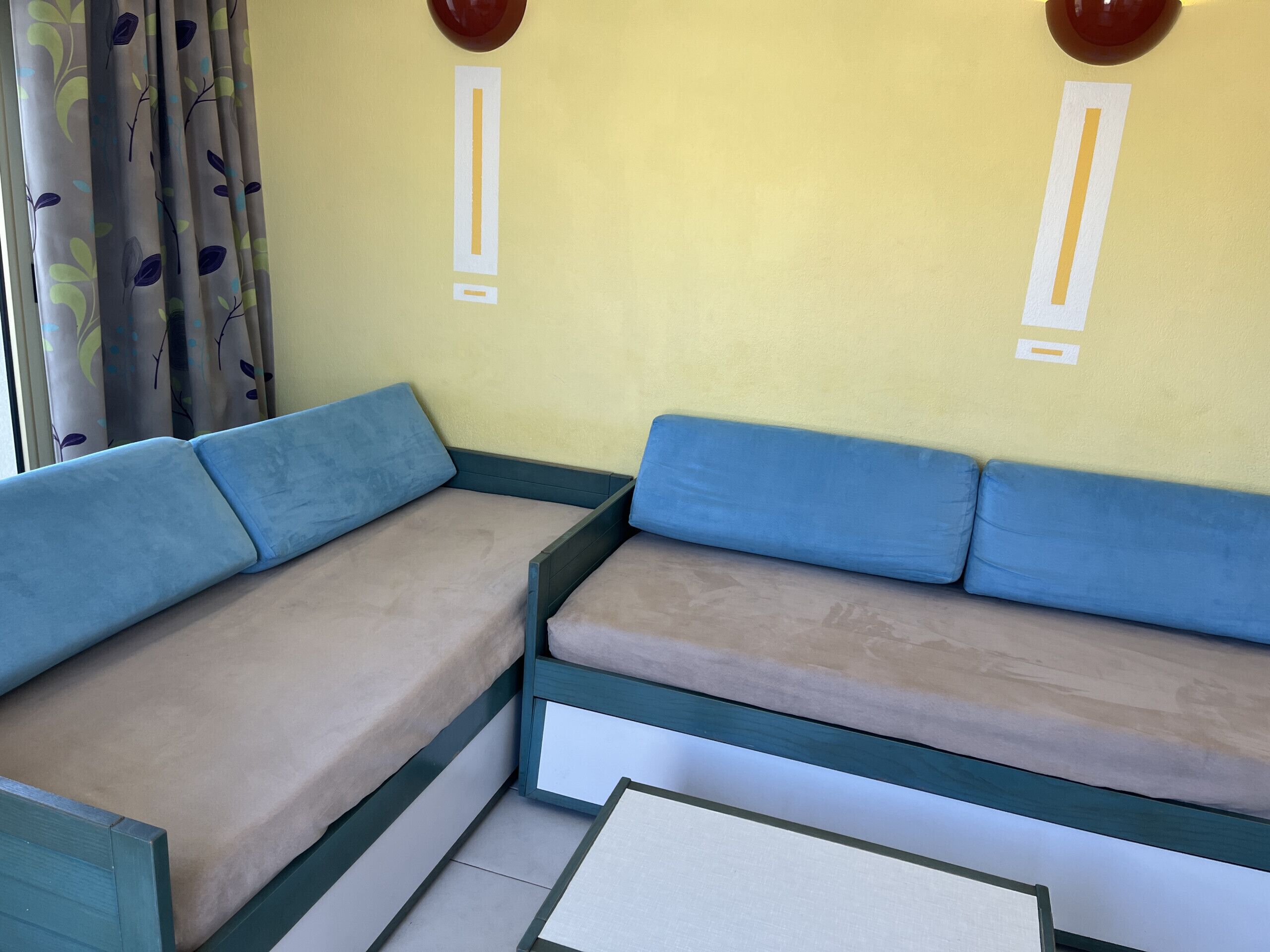 Ein Zimmer mit Schlafsofa, kleinem Tisch und einem fenster mit Vorhängen.
