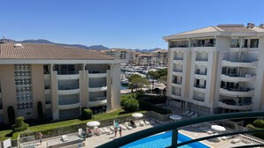 Un edificio residencial con balcones, una piscina y un puerto deportivo al fondo.