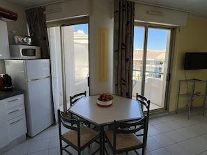 A small kitchen with a refrigerator, microwave, and a dining table with chairs. - OPEN Residence, 1-bedroom apartment (41m²), sleeps 5, close to port, beaches, swimming pool, private parking (Fréjus)