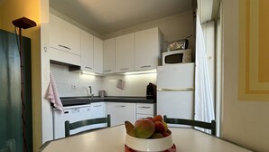 Una cocina con armarios blancos, un microondas y un bol de fruta sobre la mesa.