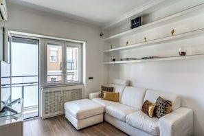 A modern living room with a white sofa, a glass coffee table, and a view of the city through large windows. - Olimpia, a luxury apartment in the heart of Monteverde in Rome (Roma)