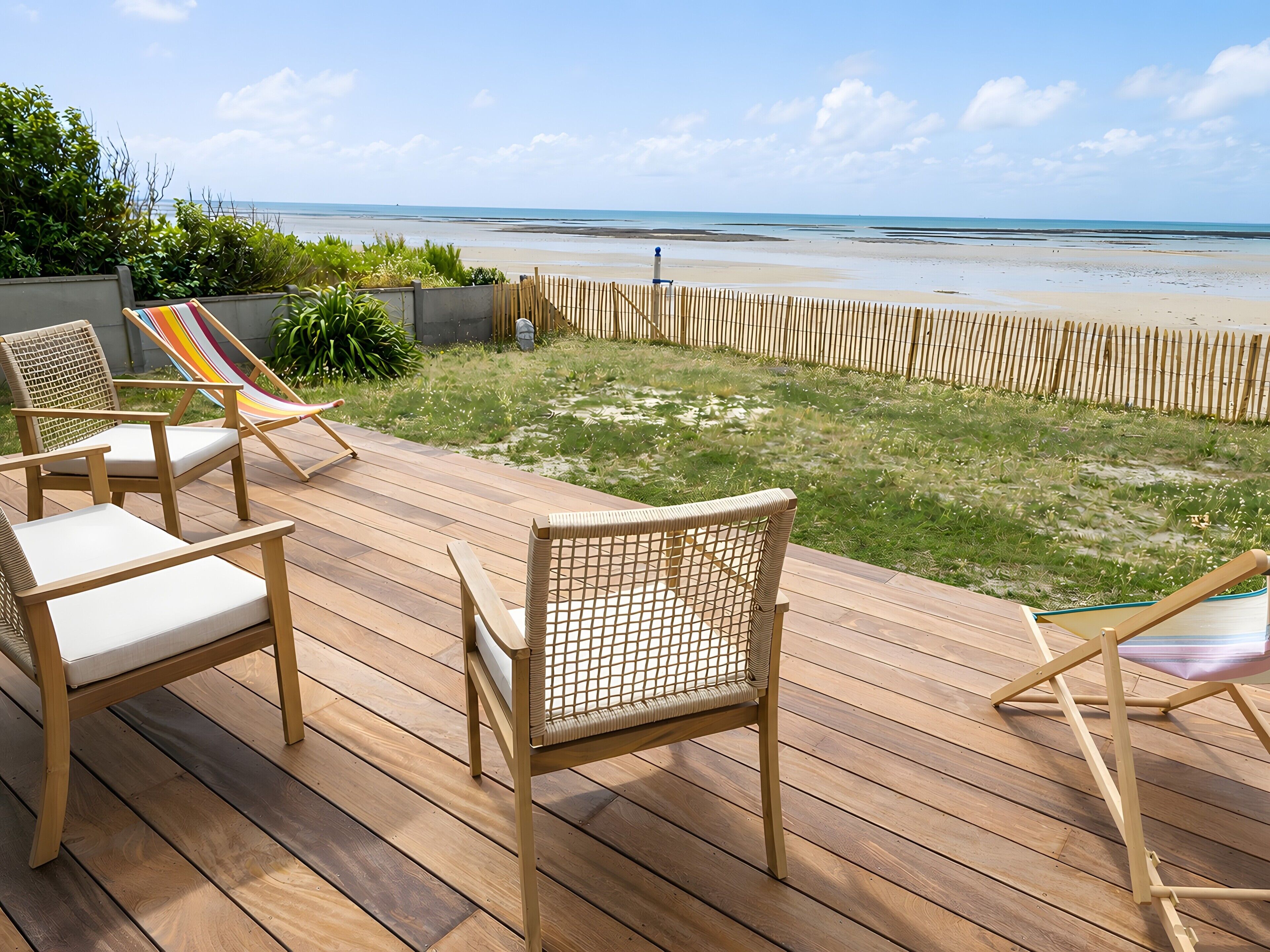 Eine Holzterrasse mit zwei Korbstühlen und einer Hängematte, mit Blick auf einen Strand.