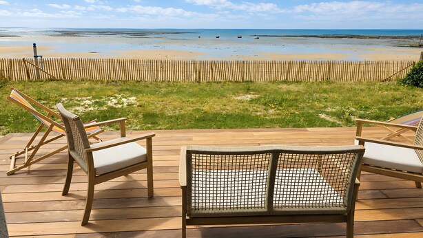 A wooden deck with two lounge chairs facing a beach.