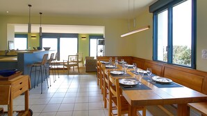 A modern kitchen with a dining area, large windows, and a view of the outdoors.