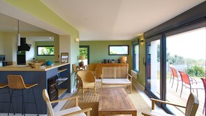 A modern kitchen with a bar area, dining chairs, a wooden table, and a large sliding glass door leading to an outdoor patio.