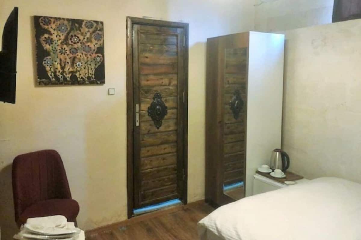 A room with a wooden door, a bed, a chair, and a painting on the wall.