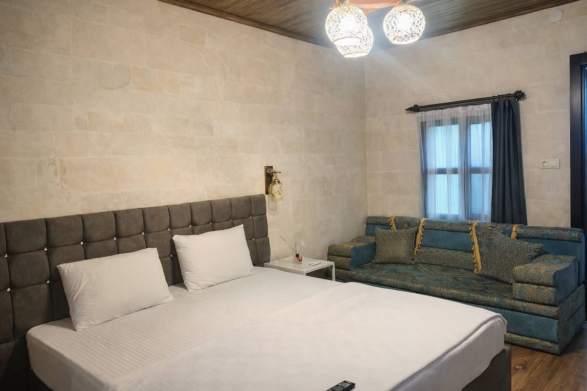 A bedroom with a bed, a sofa, a nightstand, and a wall-mounted light fixture.
