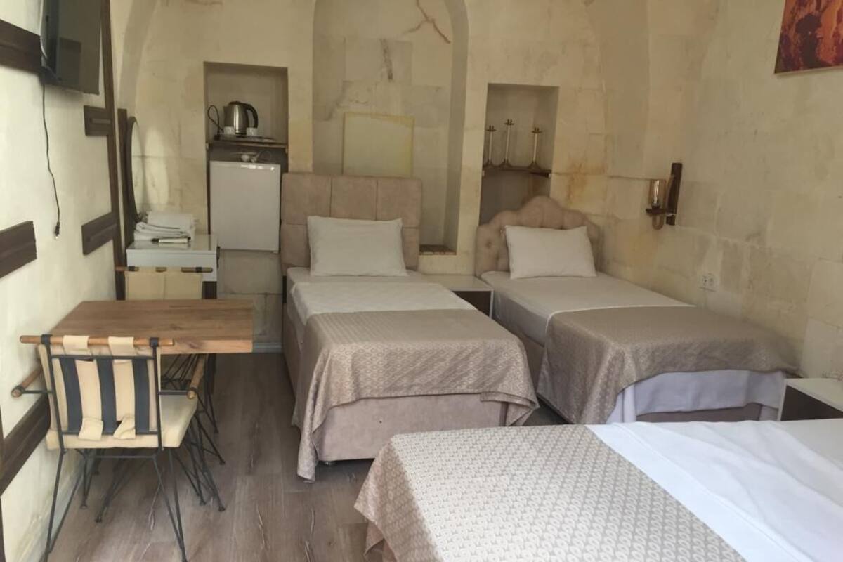 A room with two beds, a small kitchenette, a wooden table, and a TV mounted on the wall.