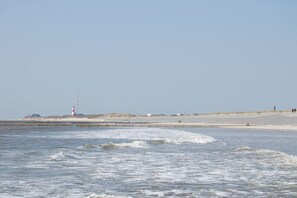 A coastal scene with a lighthouse, sandy beach, and calm sea. - Holiday home in Borkum with swimming pool (Borkum)