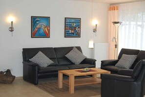 A living room with a black sofa, a wooden coffee table, and two wall-mounted lamps. - Holiday home in Borkum with swimming pool (Borkum)