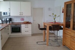 A compact kitchen with white cabinets, a microwave, a coffee maker, a toaster, and a wooden dining table with two chairs. - Holiday home in Borkum with swimming pool (Borkum)