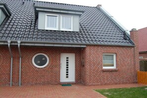 A brick house with a grey tiled roof, a circular window, and a white door. - Holiday home in Borkum with swimming pool (Borkum)