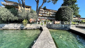 A canal with clear water, stone walls, and buildings in the background. - Villa delle Rose Apartment 66 - Private Access to the Lake (Gardone Riviera)