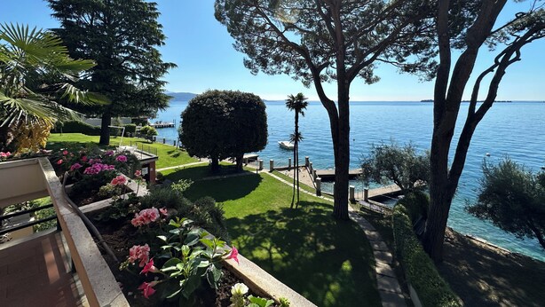 A landscaped garden with a view of the sea, a well-maintained lawn, and a variety of trees. - Villa delle Rose Apartment 66 - Private Access to the Lake (Gardone Riviera)