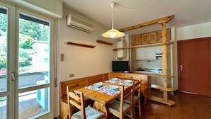 A dining area with a wooden table and chairs, a television, and a kitchen area with wooden cabinets and a stove. - Villa delle Rose Apartment 66 - Private Access to the Lake (Gardone Riviera)