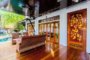 A room with a wooden floor, a sofa, a pool, and a door with decorative panels. - Darawadi Near beach 4BR Swimming pool (Sattahip)