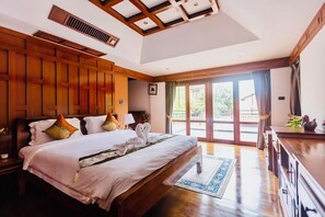 Een hotelkamer met een groot bed, houten lambrisering, uitzicht door de glazen deur en een bureau met een plant.
