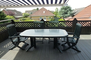 Eine überdachte Terrasse mit Tisch und Stühlen, umgeben von einer Holzterrasse und einem Gitterzaun.