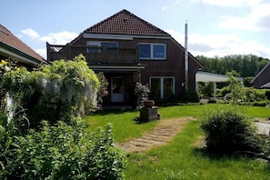 Ein zweistöckiges Haus mit Ziegelaußenwand, einem sichtbaren Schornstein und einem Garten mit gepflastertem Weg.