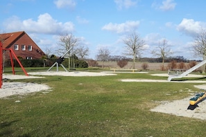 Ein Spielplatz mit Schaukeln und Rutschen, eine rote Konstruktion und ein Gebäude im Hintergrund.