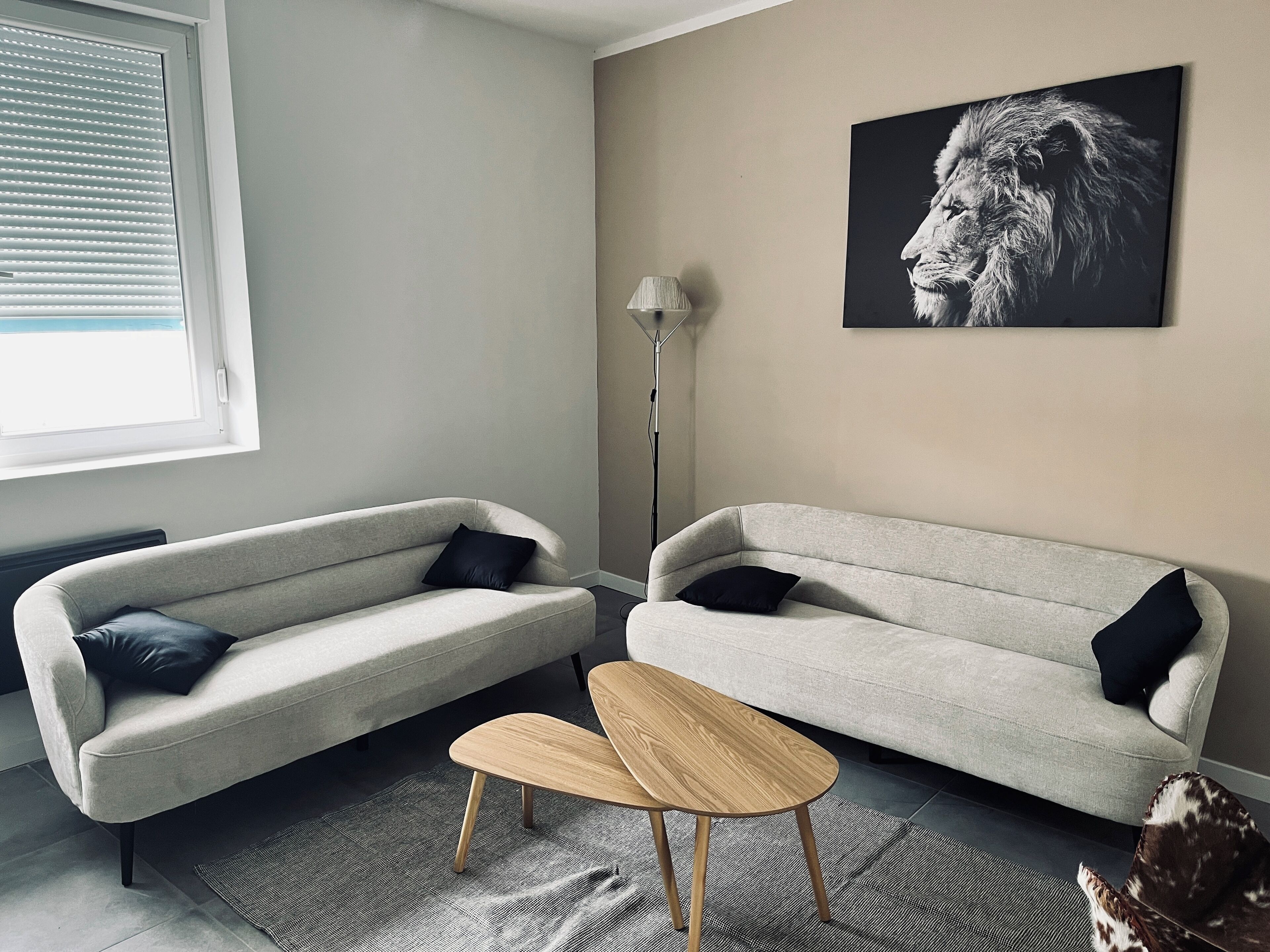 A living room with two sofas, a small wooden table, a zebra-patterned rug, a floor lamp, and a lion portrait on the wall.