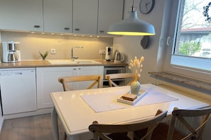 A modern kitchen with white cabinets, a dishwasher, a coffee maker, and a dining table with chairs. - Holiday home with 3 bedrooms (Wangerland\/Horumersiel\/Schillig)