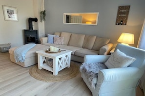 A living room with a sofa, a chair, a small table with candles, a fireplace, and a mirror on the wall. - Holiday home with 3 bedrooms (Wangerland\/Horumersiel\/Schillig)
