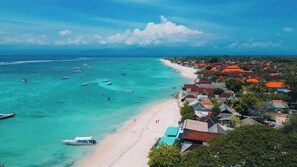 Eine Küstenlandschaft mit Strand, Booten und einer Reihe Häuser mit roten Dächern.