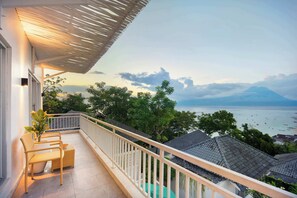 Ein Balkon mit Korbmöbeln, Blick auf das Meer und ein Berg in der Ferne.