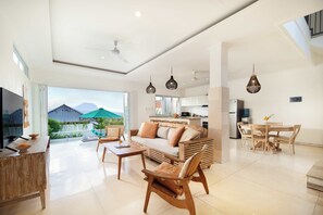 Ein geräumiger Wohnbereich mit Sofa, Couchtisch und Esstisch, einem Fernseher und einer Küche im Hintergrund.