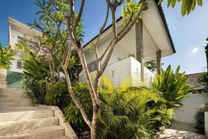 Ein Wohngebäude mit einer Treppe, die zu einer überdachten Veranda führt, umgeben von üppiger Vegetation.