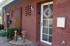 A brick building with a wooden door, a glass door, and a wreath on the right. - Frisian happiness in Greetsiel (Greetsiel)